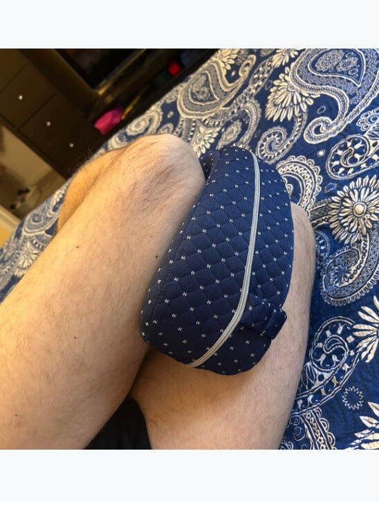 Review photo: the navy knee pillow held between the legs on a patterned bedspread